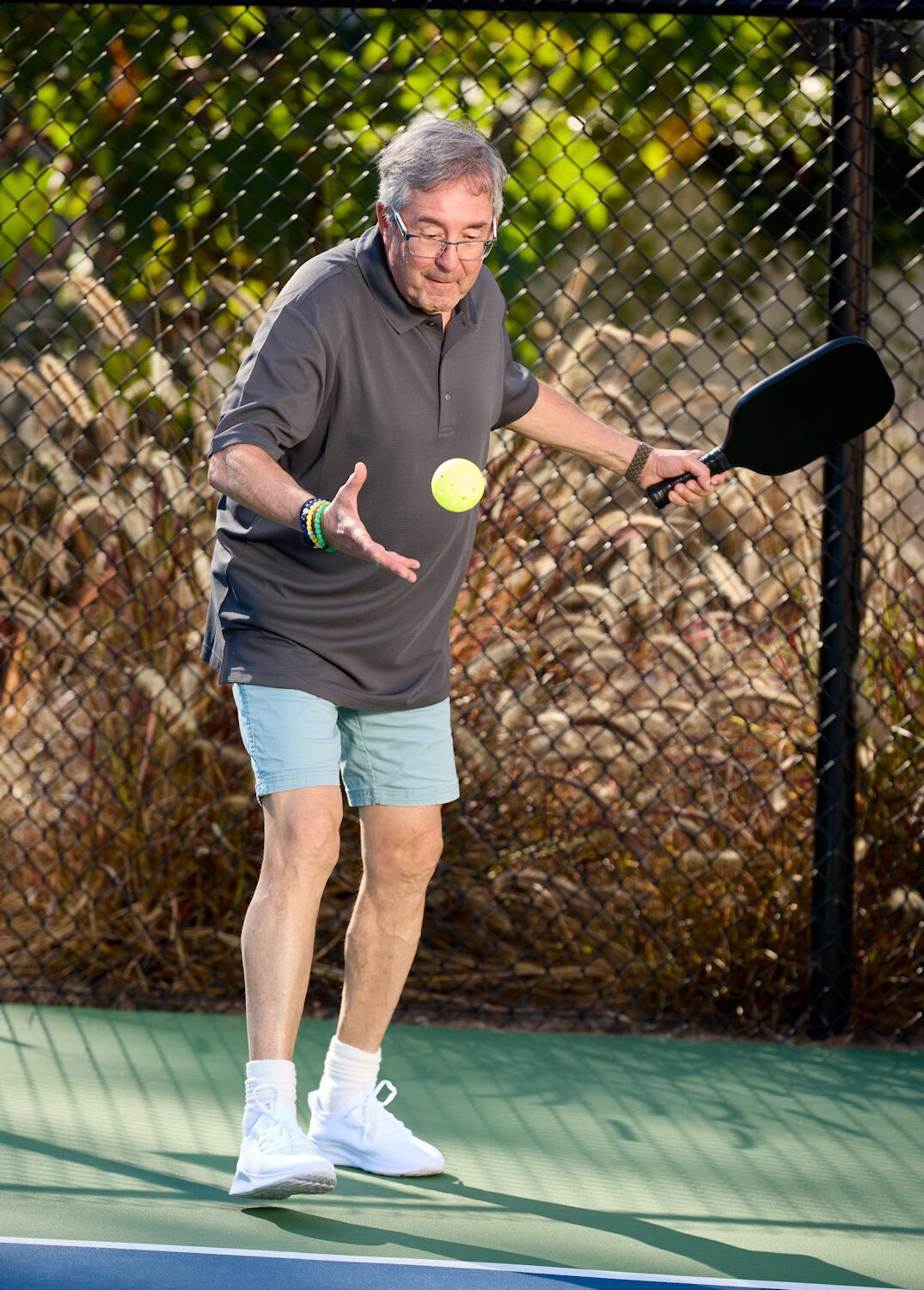 older man plays pickleball on a blue court